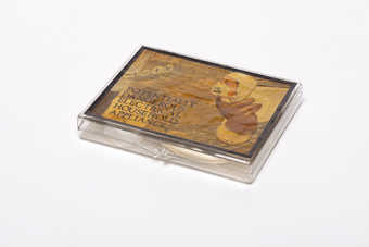A hinged plastic box with attached paper label with vinyl border covered with varnish?. Inside of...