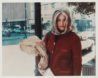 Photograph of Roberta carrying a brown bag, wearing red jacket.
