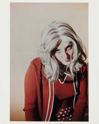 Image of Roberta sitting with head dipped towards the camera, wearing red top and red skirt with...