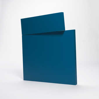 A blue geometric sculpture in which a smaller rectagular form rests at an angle on top of a...