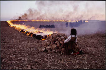 An image of a child crouched behind a mound of stones, from which a fire "fence"...