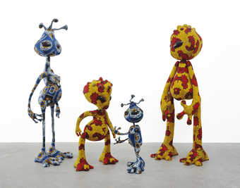 Three standing alien figures constructed of stuffed wax printed fabric.