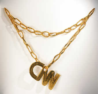 An oversize necklace and pendant "CNN' constructed of gold wrapped cardboard