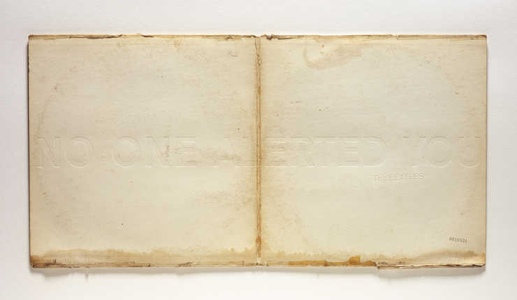 An unfolded copy of the Beatles White Album embossed with the phrase "NO ONE ALERTED YOU"