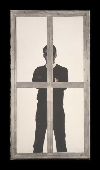 A black-and-white image of a man standing behind a painting stretcher.