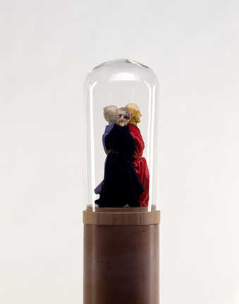 wood base has three fimo clay figures with different colored clothing, tied together with brass...